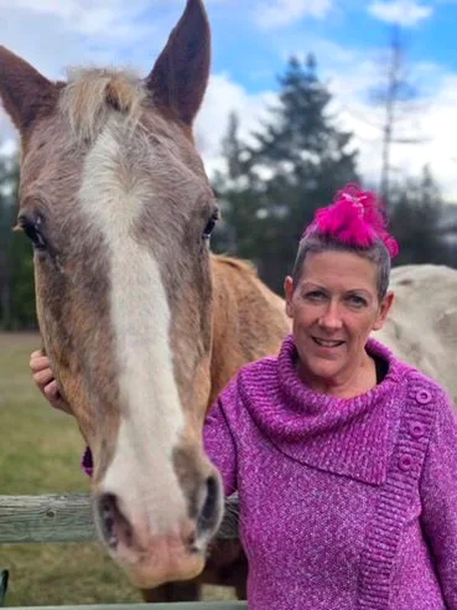 Raven Addison standing beside a horse at a wooden fence on the property
