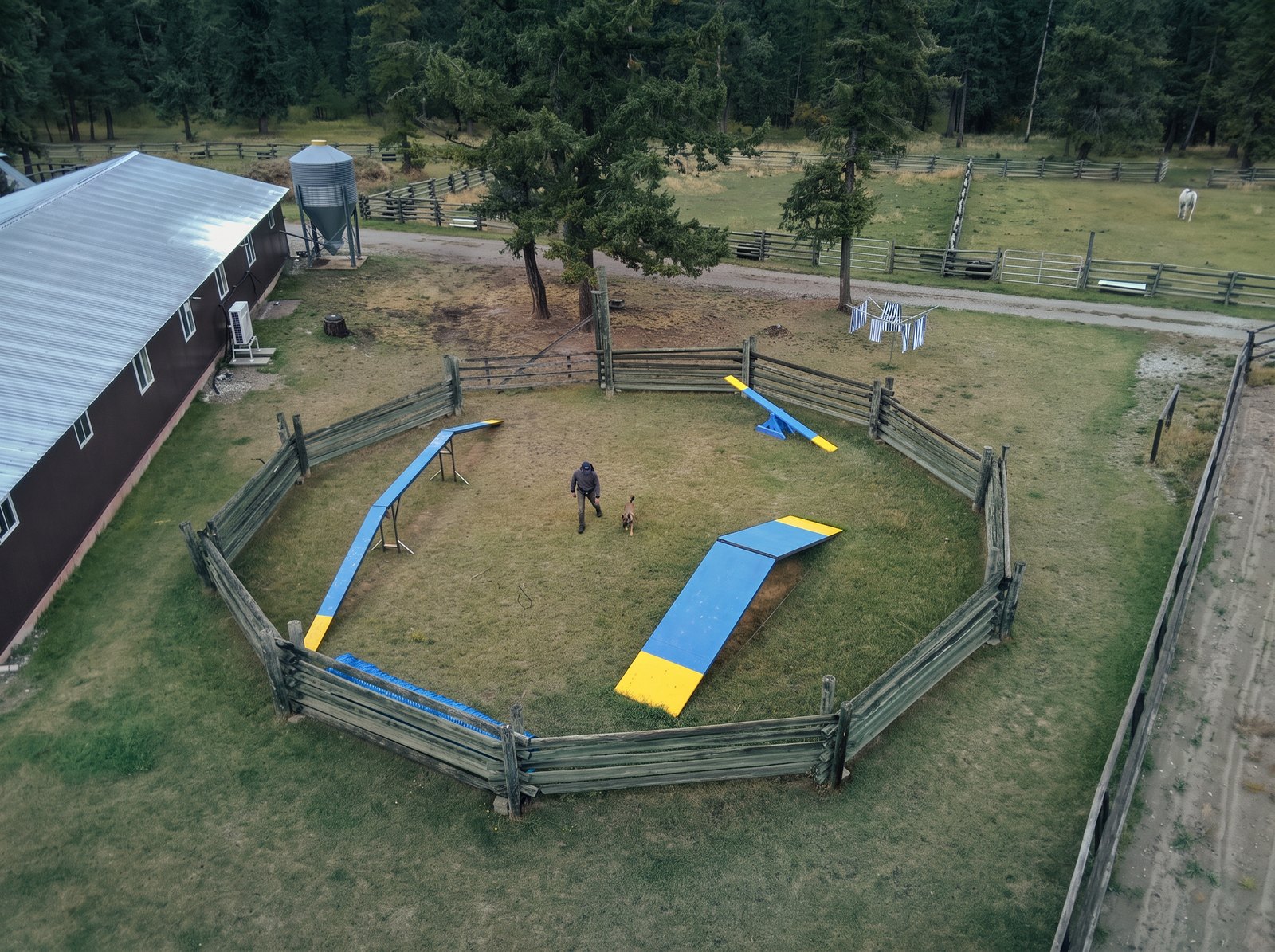 Aerial view of a handler and dog inside the fenced agility training area at K9 Basecamp
